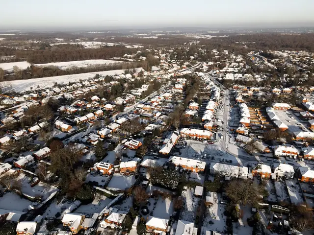 Snow and frost lying on suburban rooftops below wooded downland on a cold winter morning in Surrey