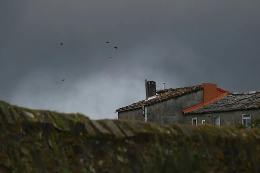 A house roof under heavy storm clouds of the kind that lead to insurance claims