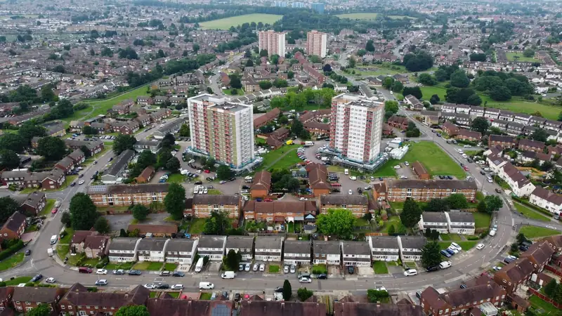 Aerial view of a postwar housing estate with rows of concrete tiled semis and terraces around two tower blocks