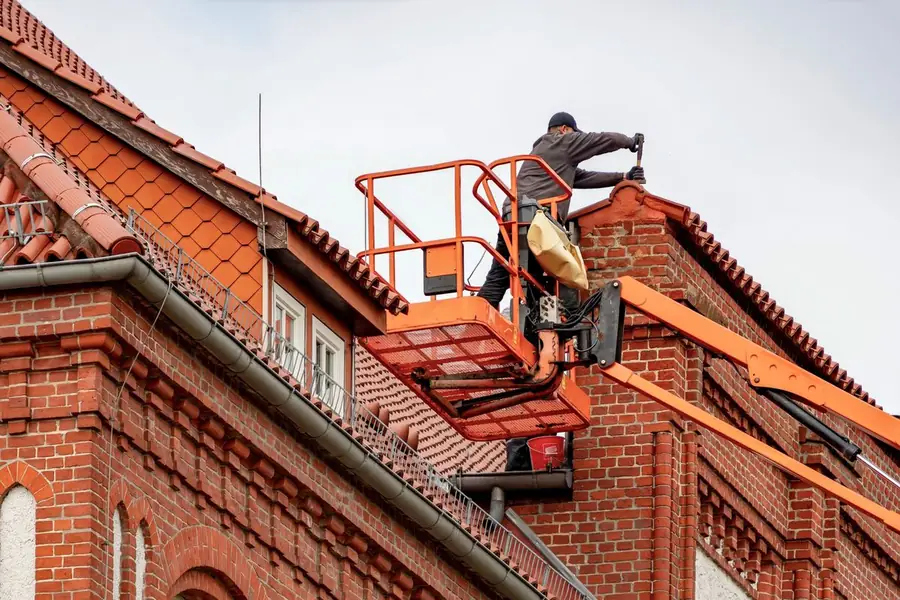 A roofer on a cherry picker repairing a red brick house before it goes on the market