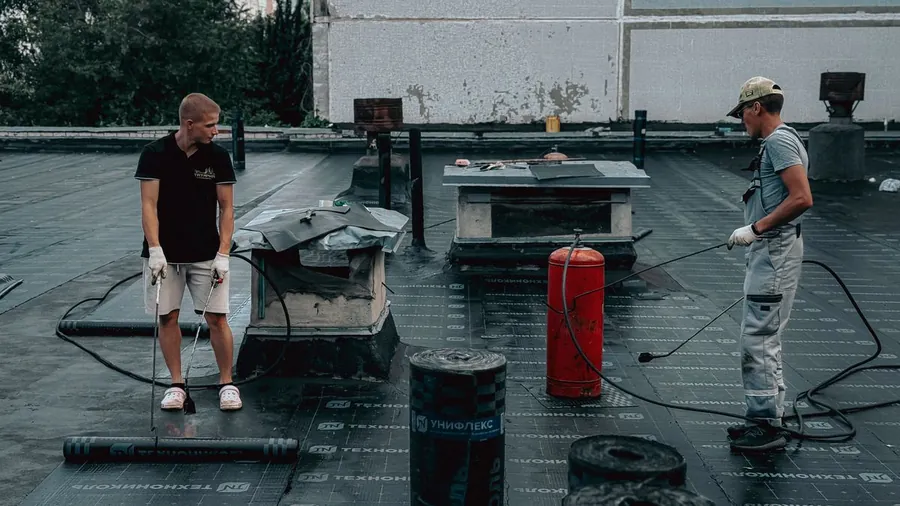 Roofers working on a torch-on felt flat roof in summer heat