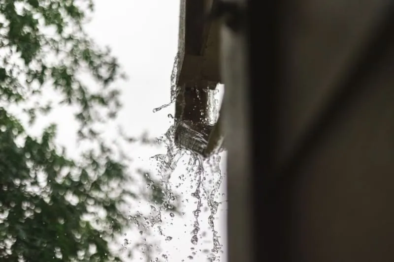 Water pouring off the edge of a roof past a failed gutter on a house in Croydon